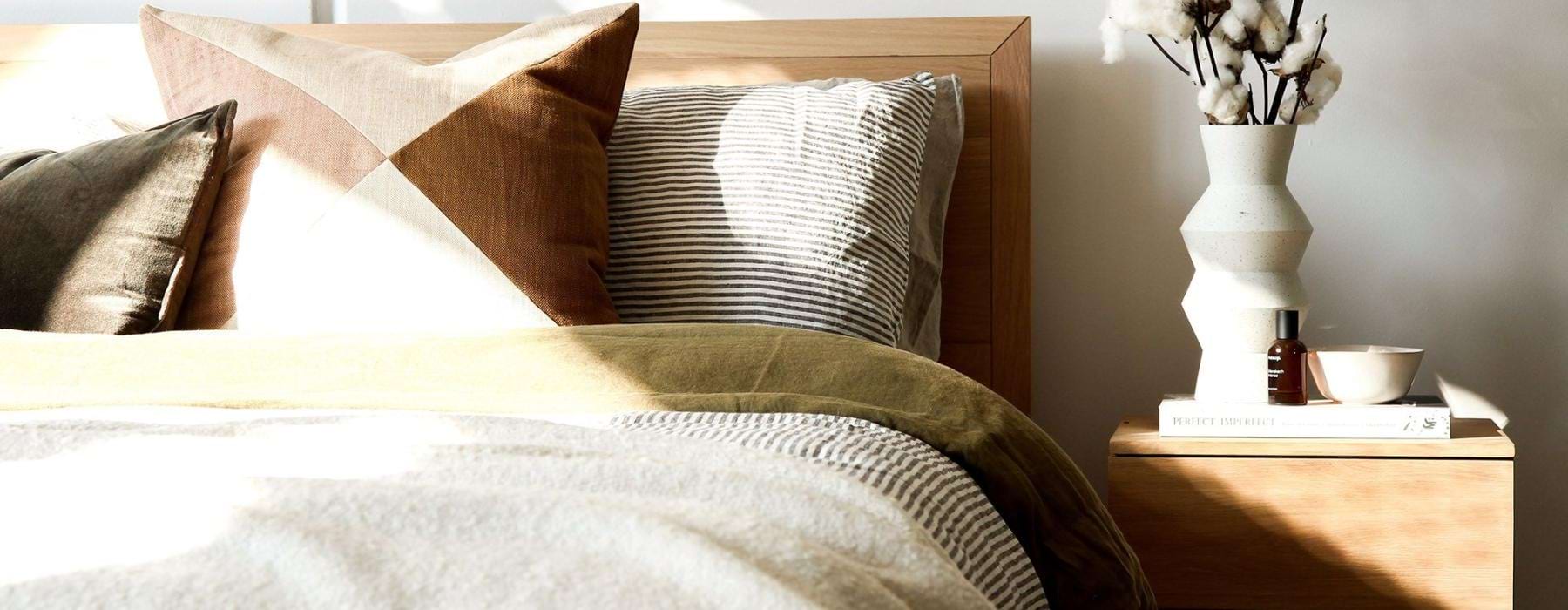 swath of sunlight shines across a well made bed and bedside table with a vase of cotton plants